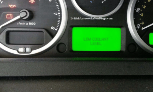 Car dashboard with a green display reading “LOW COOLANT LEVEL” between gauges.