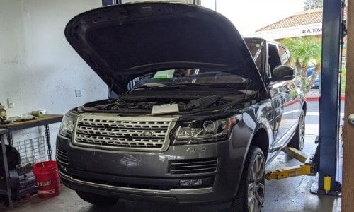 Black Range Rover in a garage with its hood open, showing the engine bay.
