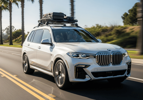 White BMW SUV driving on a sunny palm-lined road with luggage on the roof
