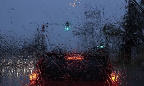 Rain-streaked windshield at dusk, with red brake lights and a green traffic signal ahead.