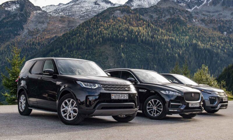 Three black SUVs parked side by side with mountains in the background