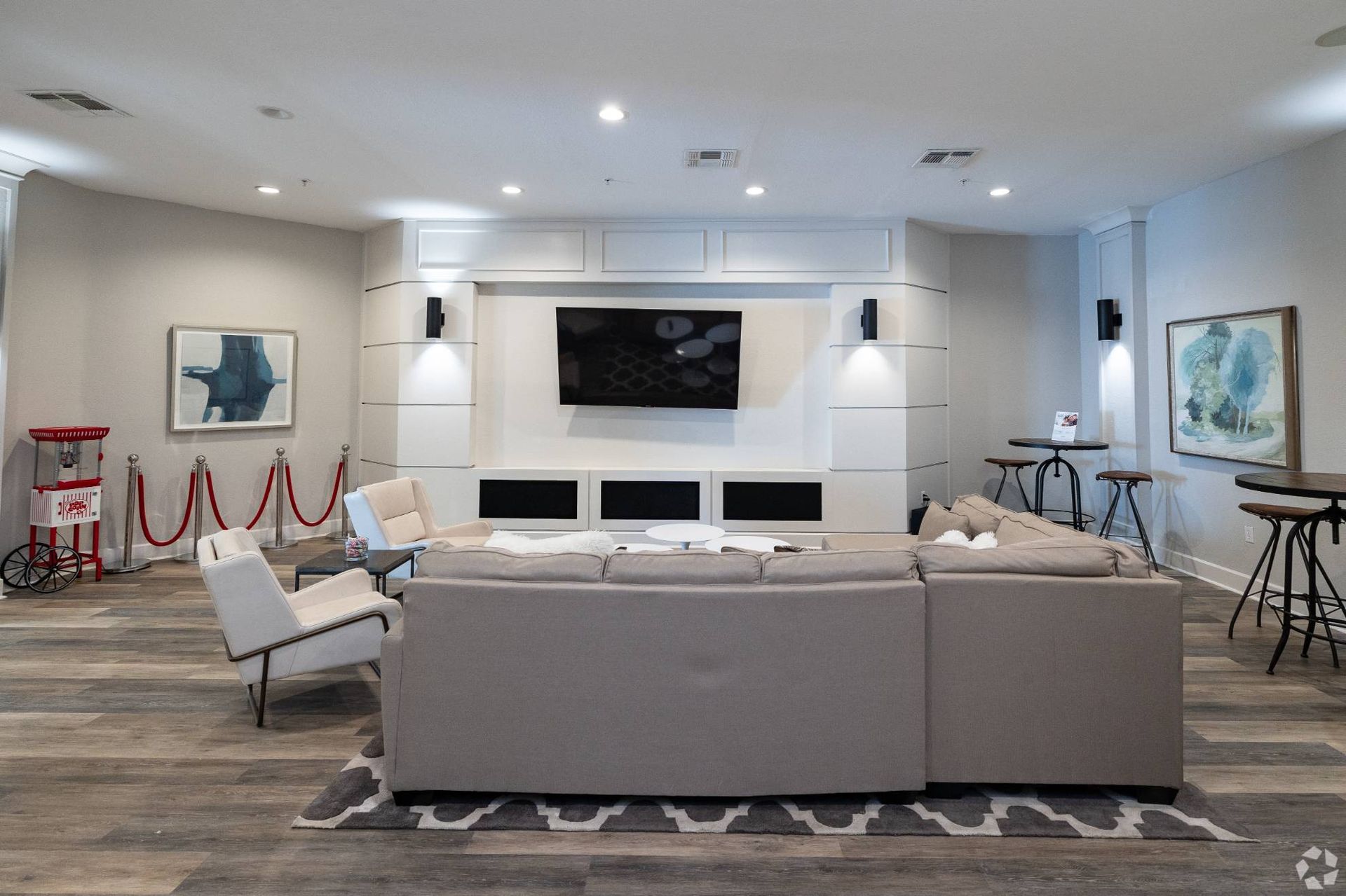 Communal apartment lounge with a large sectional sofa, wall-mounted TV, and high-top tables.