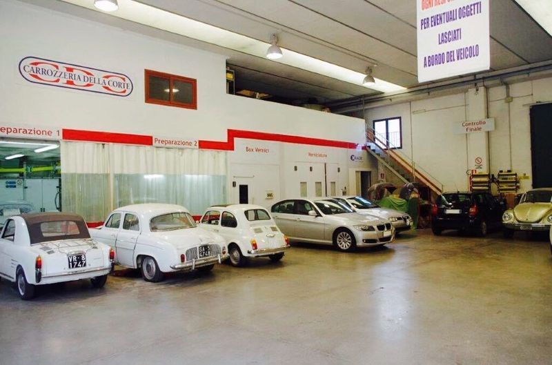 Interno di un'officina meccanica con diverse auto parcheggiate e un meccanico al lavoro in fondo alla stanza.