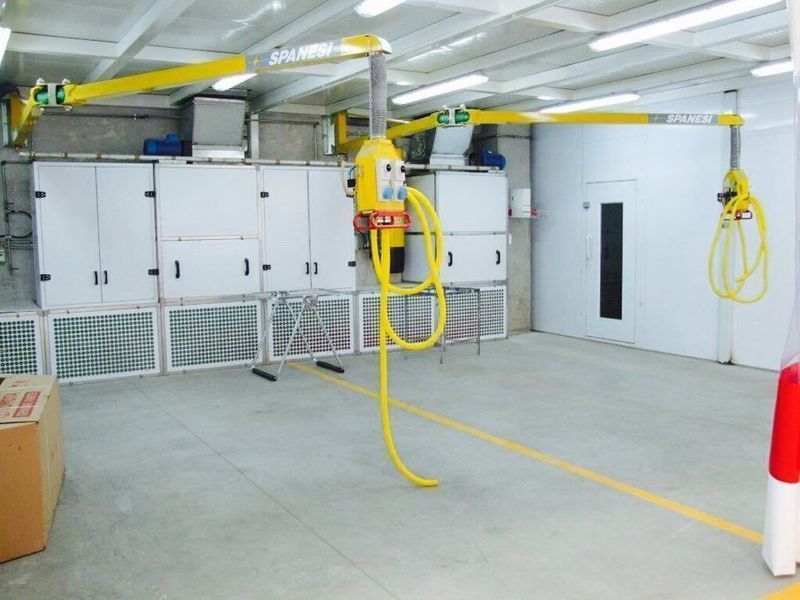 Locale industriale con armadi di controllo bianchi, paranchi gialli e tubi flessibili appesi al soffitto.
