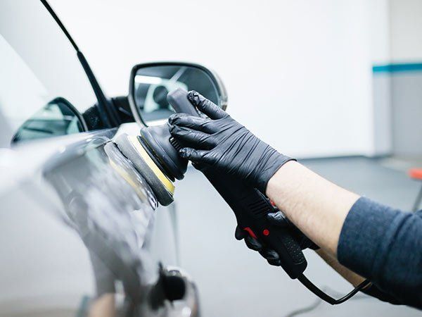 Una persona lucida una portiera e uno specchietto laterale di un'auto con una lucidatrice elettrica in un garage.