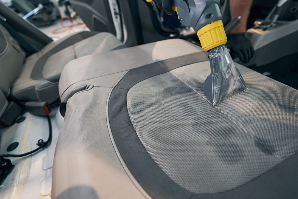 Pulizia con ugello aspirapolvere del rivestimento grigio di un sedile auto all'interno di un veicolo
