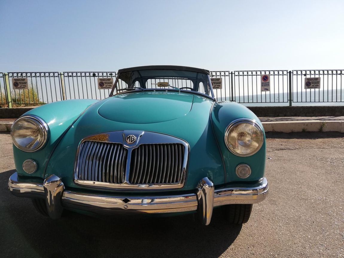 Auto d'epoca turchese parcheggiata vicino alla ringhiera del lungomare in una giornata di sole.