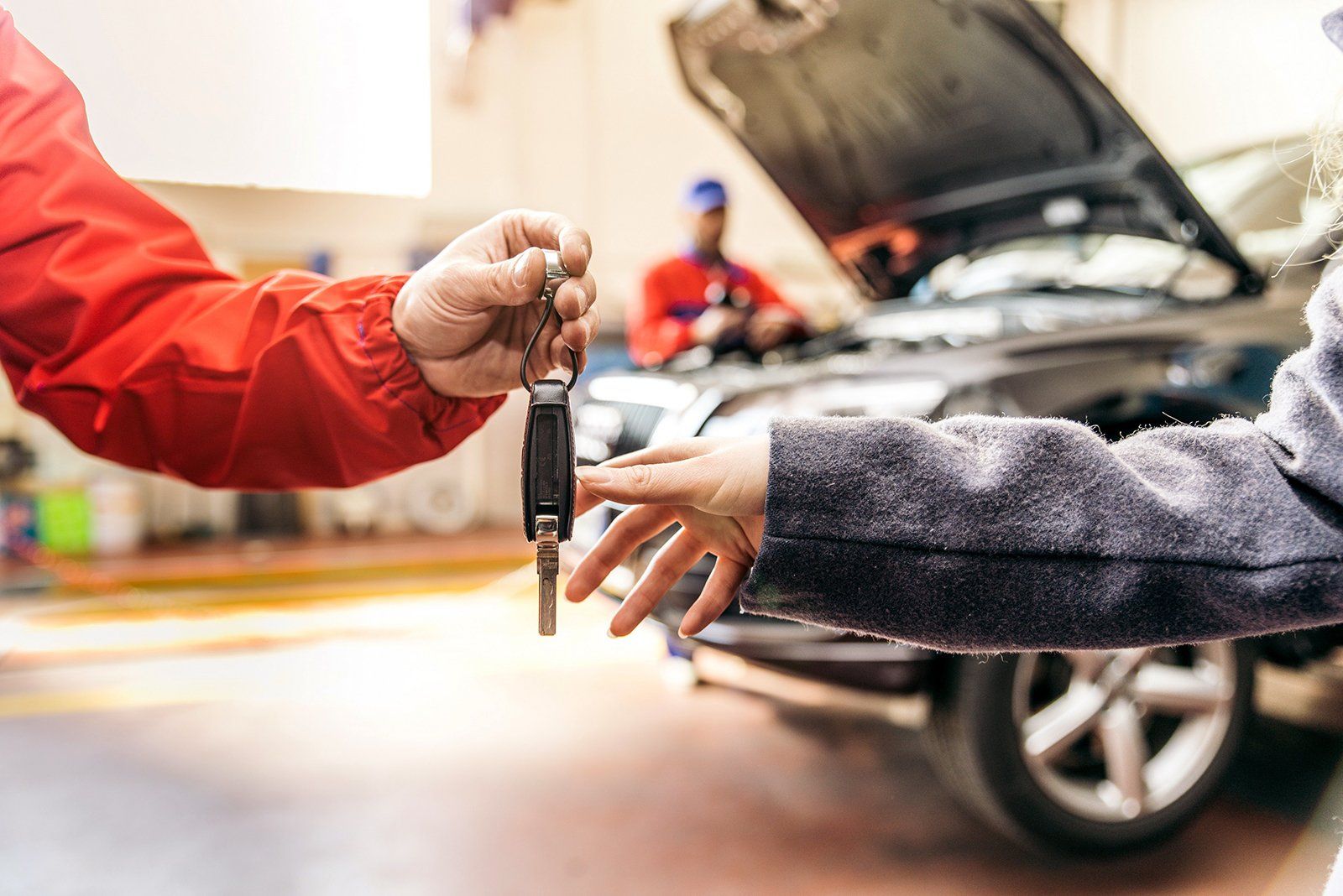 Una chiave dell'auto viene consegnata a una persona accanto a un'auto con il cofano aperto in un'officina.
