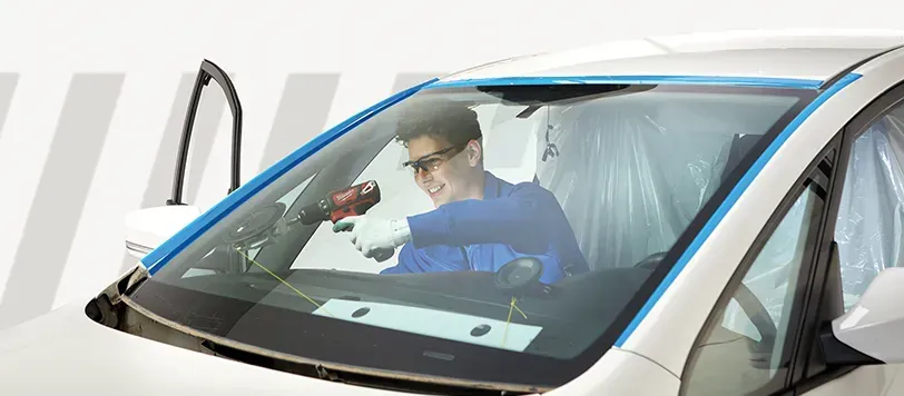 Un automobilista con la giacca blu si protende verso un oggetto rosso all'interno del parabrezza di un'auto.