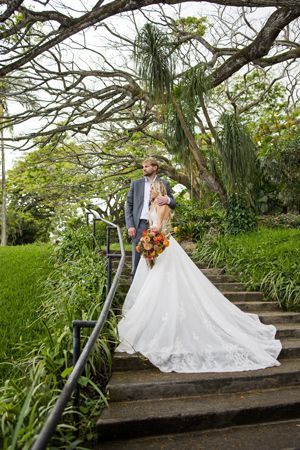 A Bride And Groom Are Standing On A Set Of Stairs In A Park - Honolulu, HI - Bella Rosa Corporation