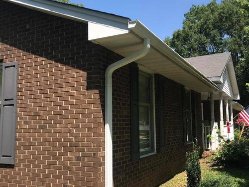 Brick house exterior with white gutters, windows, and a shaded front porch