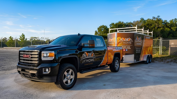 Black pickup truck towing an orange utility trailer parked on a sunny roadside.