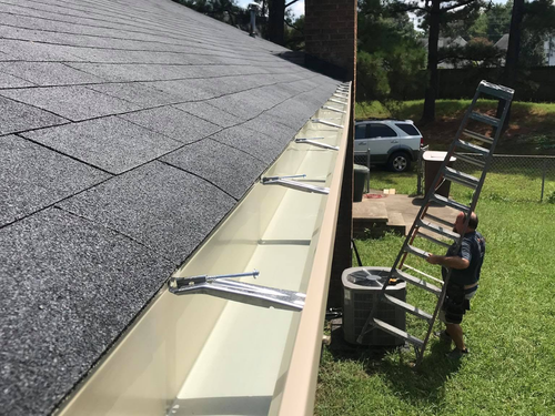 Gutter installation along a roof edge with two workers on a ladder below