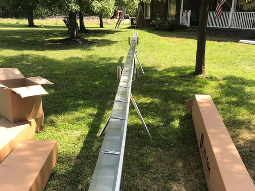 Long metal trough set up outdoors on a grassy lawn with cardboard boxes nearby.