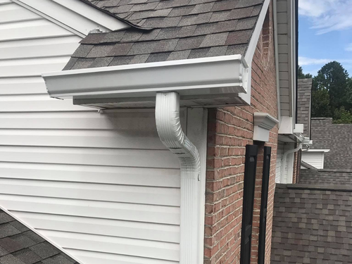 Roof gutter and downspout on a brick house with white siding and gray shingles