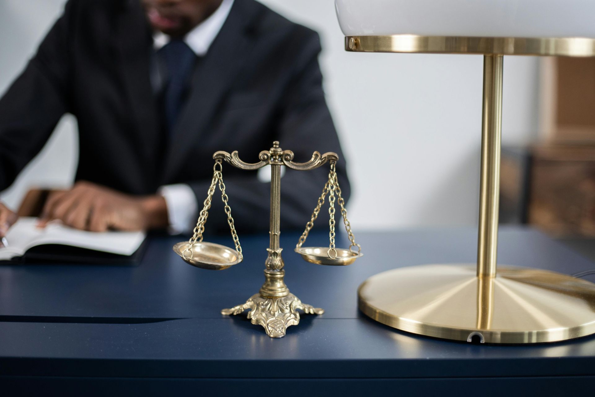 Gold scales of justice on a desk with a blurred lawyer in the background