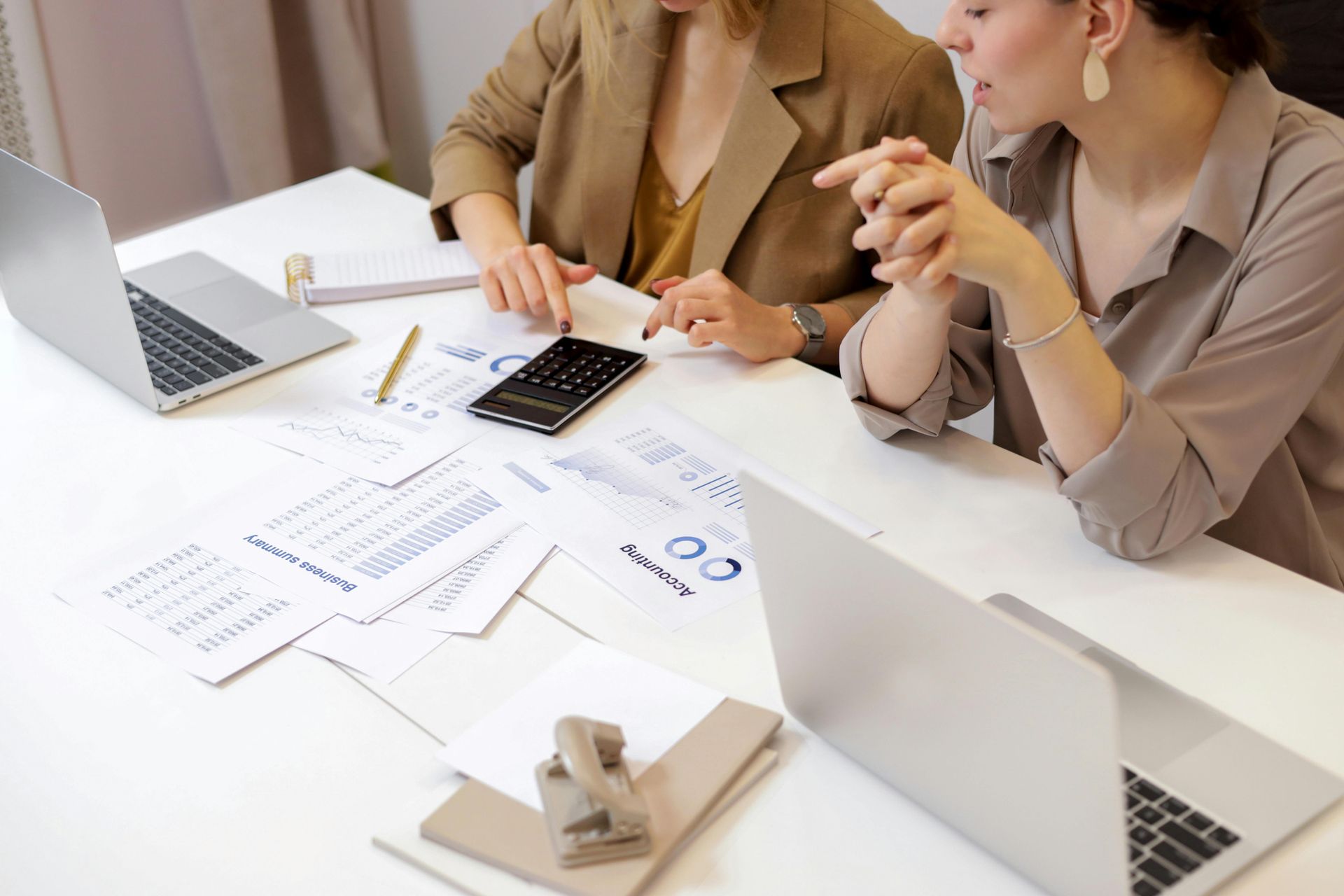 Two people review documents at a desk with laptops and a calculator.