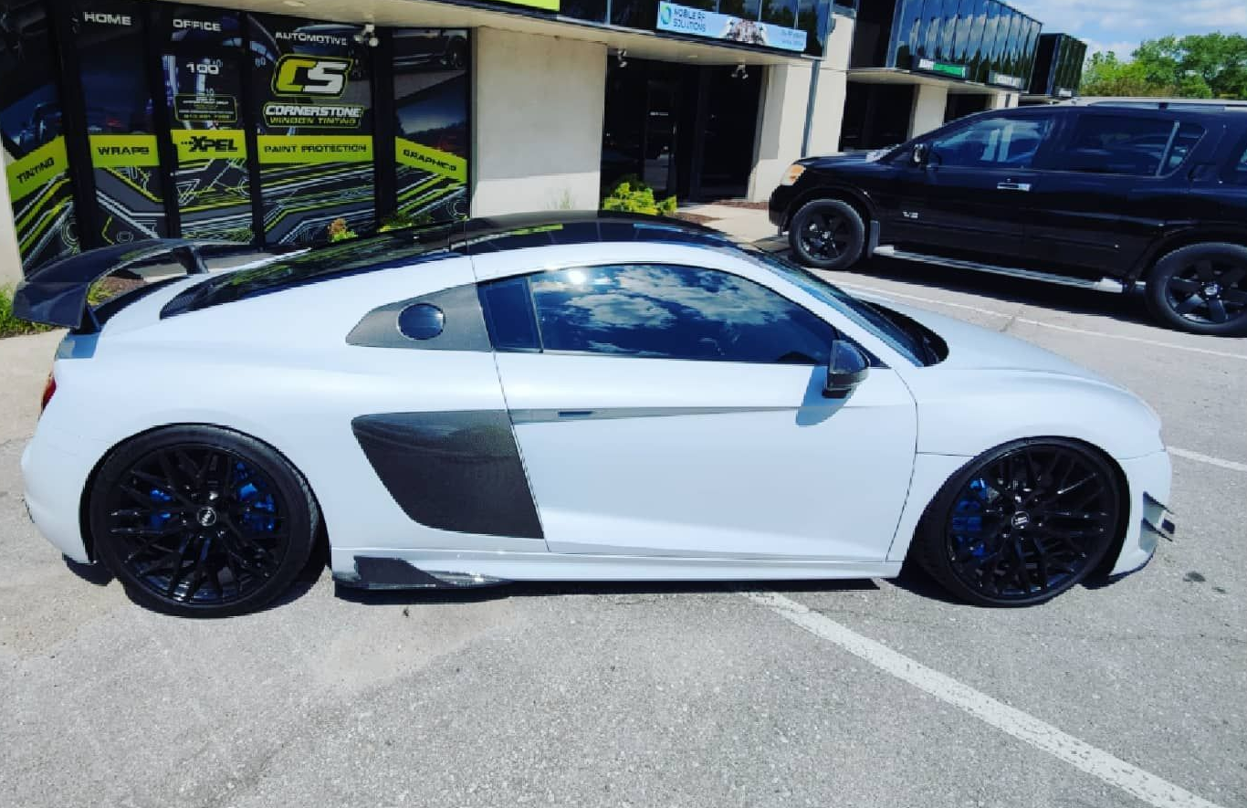 Light gray Audi R8 sports car with black accents and wheels parked outside a building.
