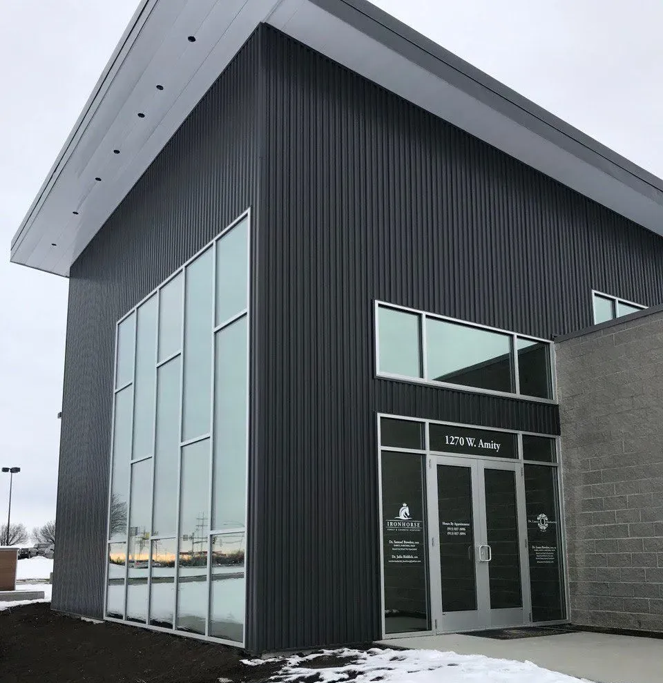 Modern building with dark gray siding, large windows, and a sloping white roof. Snow on the ground.