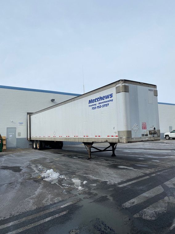 A white trailer is parked in a parking lot in front of a building.
