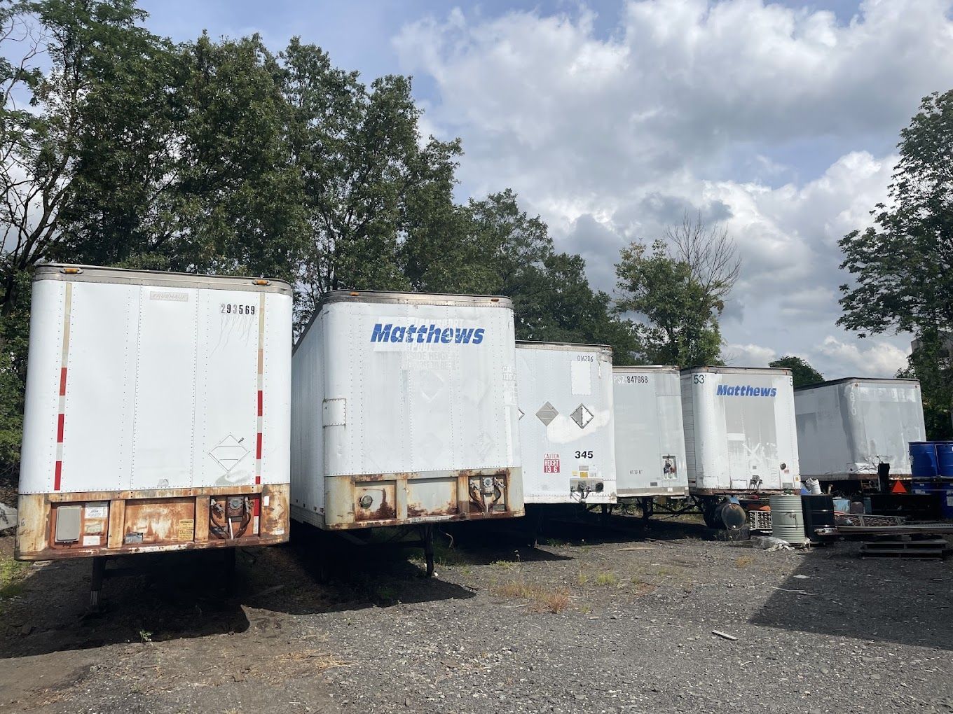 A row of white trailers are parked in a gravel lot.