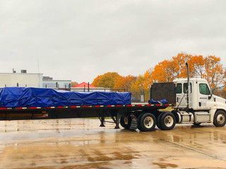 A semi truck with a blue tarp on the back is parked in a parking lot.