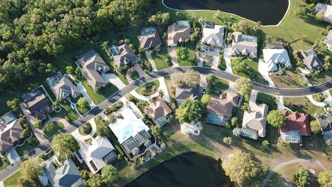 Aerial view of a suburban neighborhood with houses, trees, winding streets, and a pond.