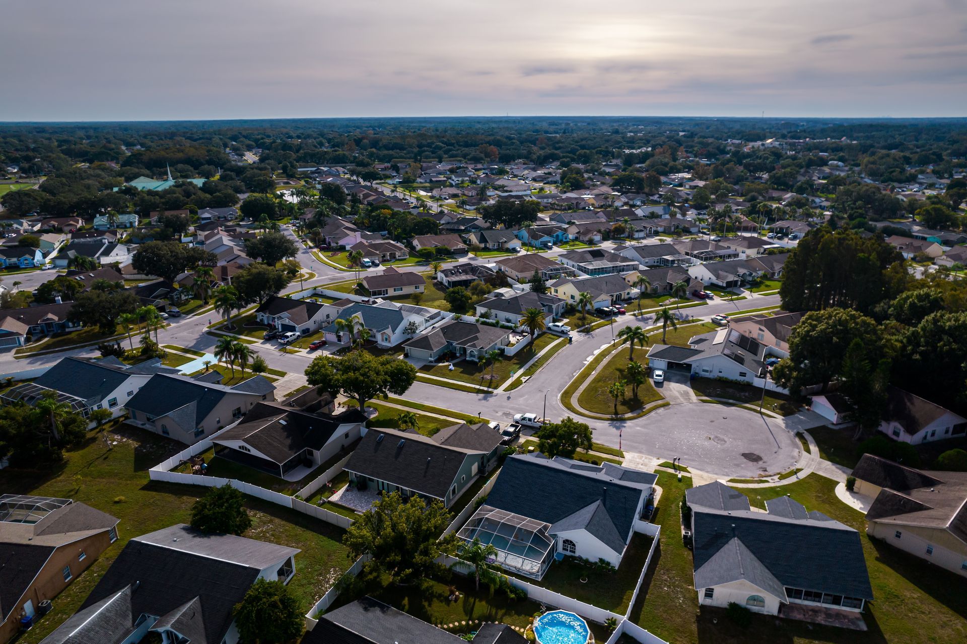 Aerial view of a suburban neighborhood with houses, streets, and trees at sunset.