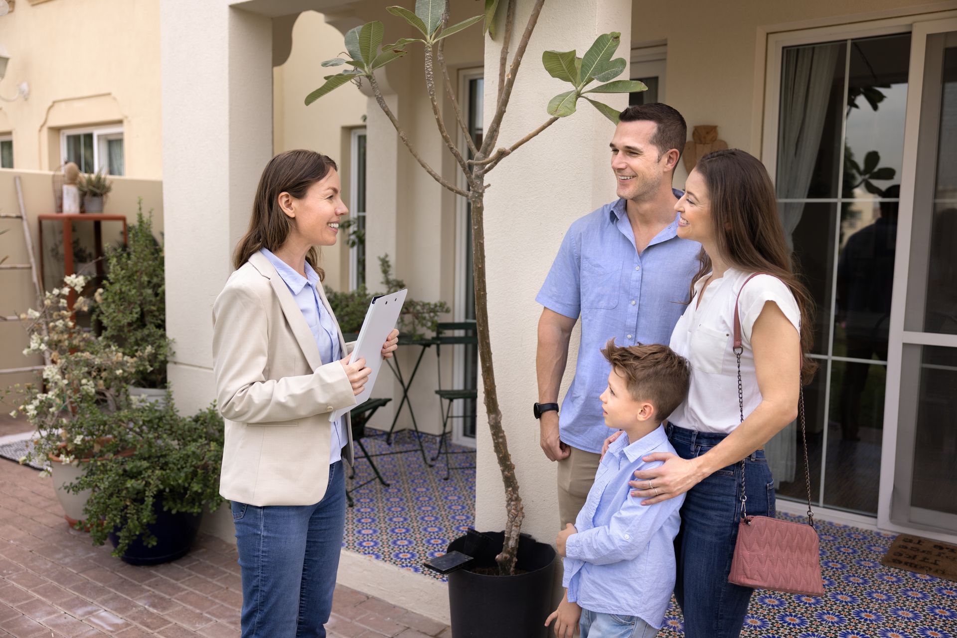 Two adults and a child talking outside a house, with one person holding a pink purse.