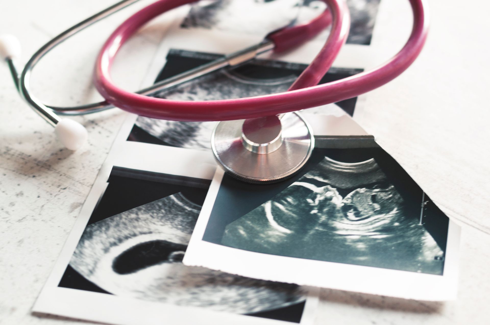 Pictures of an ultrasound with a pink stethoscope on top of them, showcasing prenatal care.