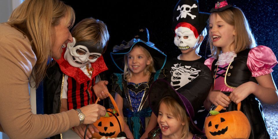 A woman is giving candy to a group of children dressed in halloween costumes.