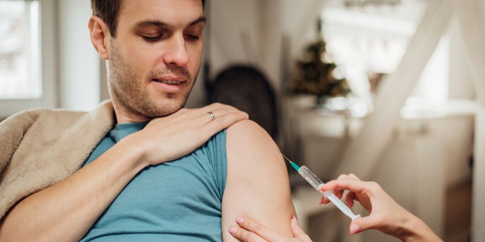 A man is getting an injection in his arm while sitting on a couch.