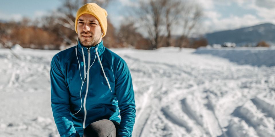 A man in a blue jacket and yellow hat is sitting in the snow.