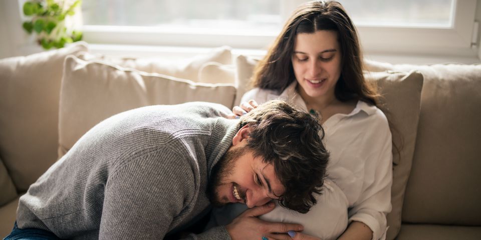A man is kneeling down next to a pregnant woman on a couch.