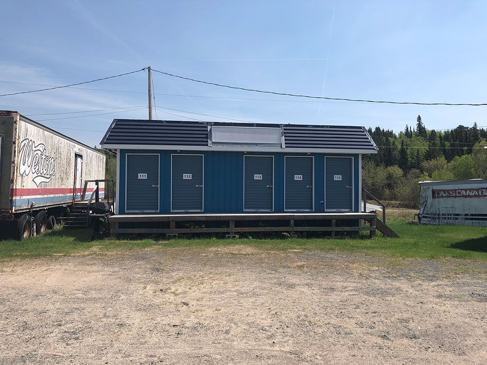 A small blue building with four doors is sitting in the middle of a dirt field.