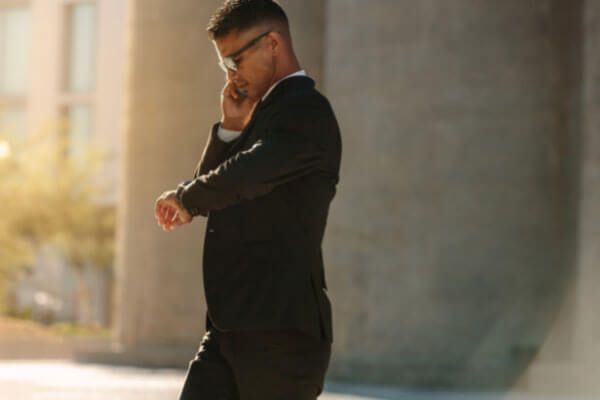 A man in a suit is talking on a cell phone while looking at his watch.
