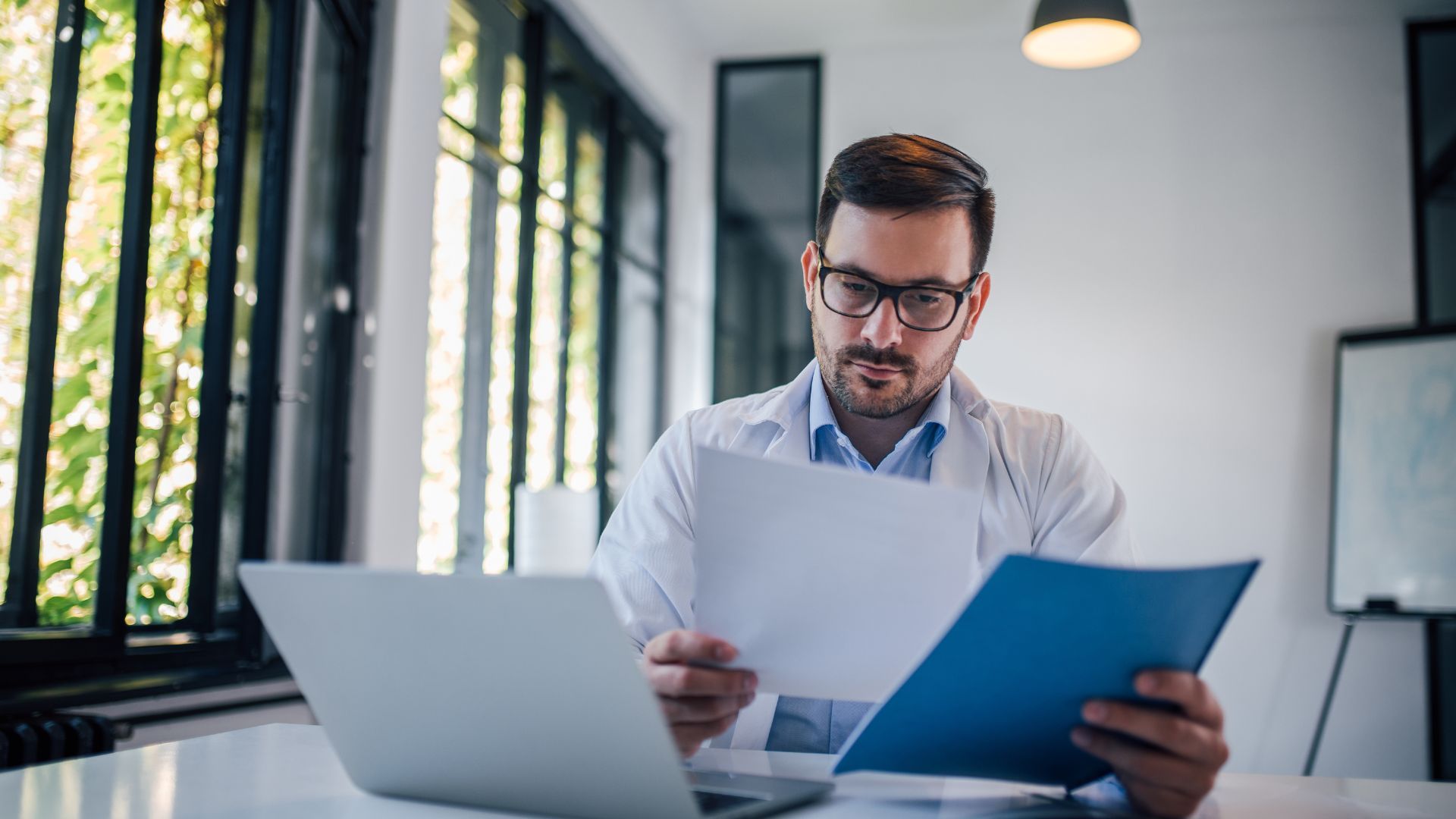 A man is sitting at a table with a laptop and a clipboard.