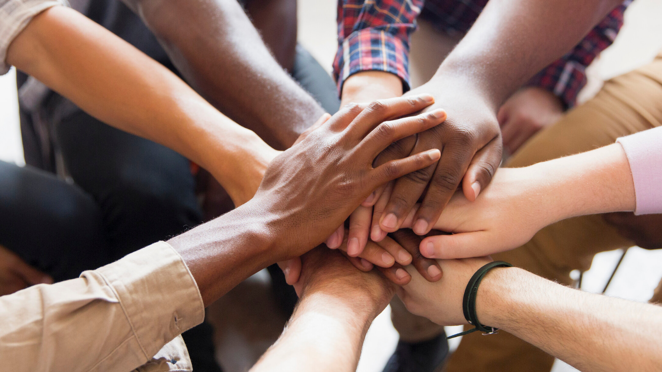 A group of people place their hands together in the center in a gesture of unity and teamwork.