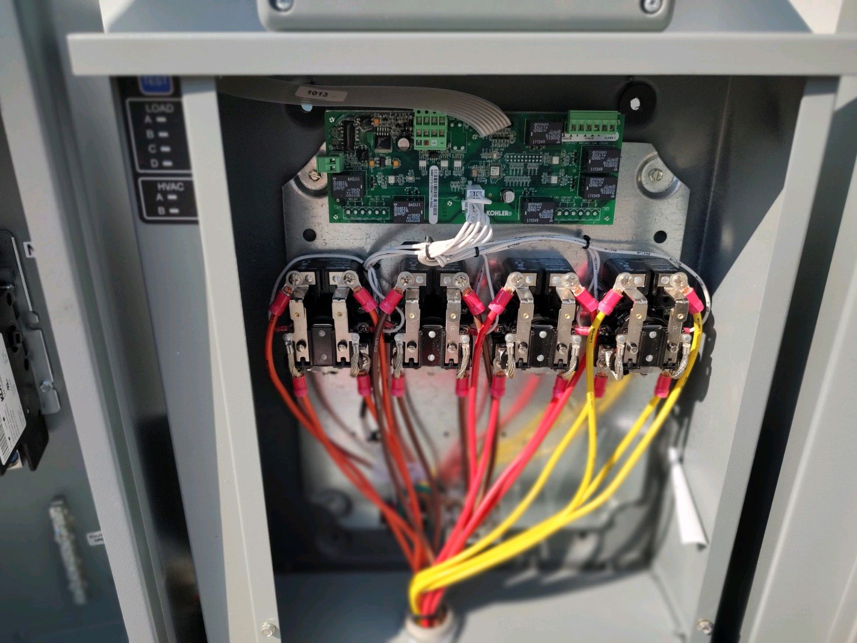 Electrical panel interior, showing circuit breakers with colored wires and a circuit board.
