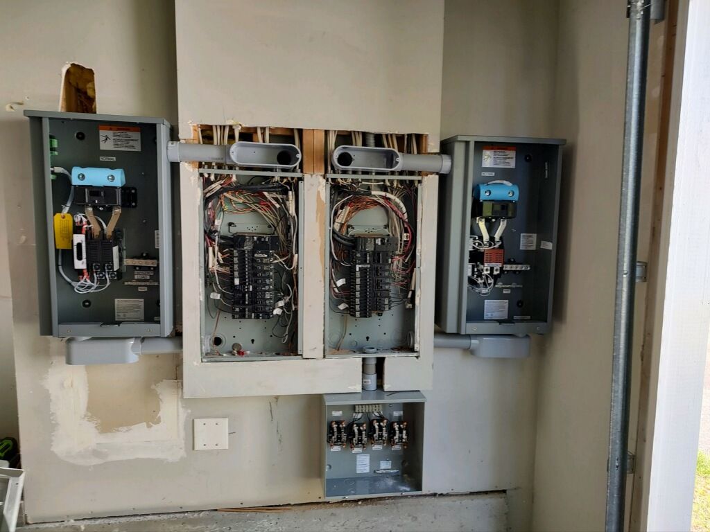 Electrical panels and conduit mounted on a wall. Several gray metal boxes house circuit breakers and other components.