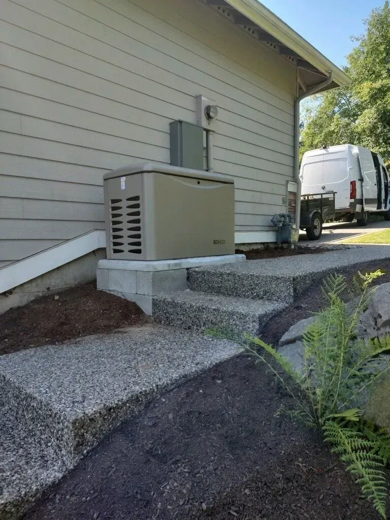 A beige generator unit next to a house, with concrete steps and a van parked nearby.