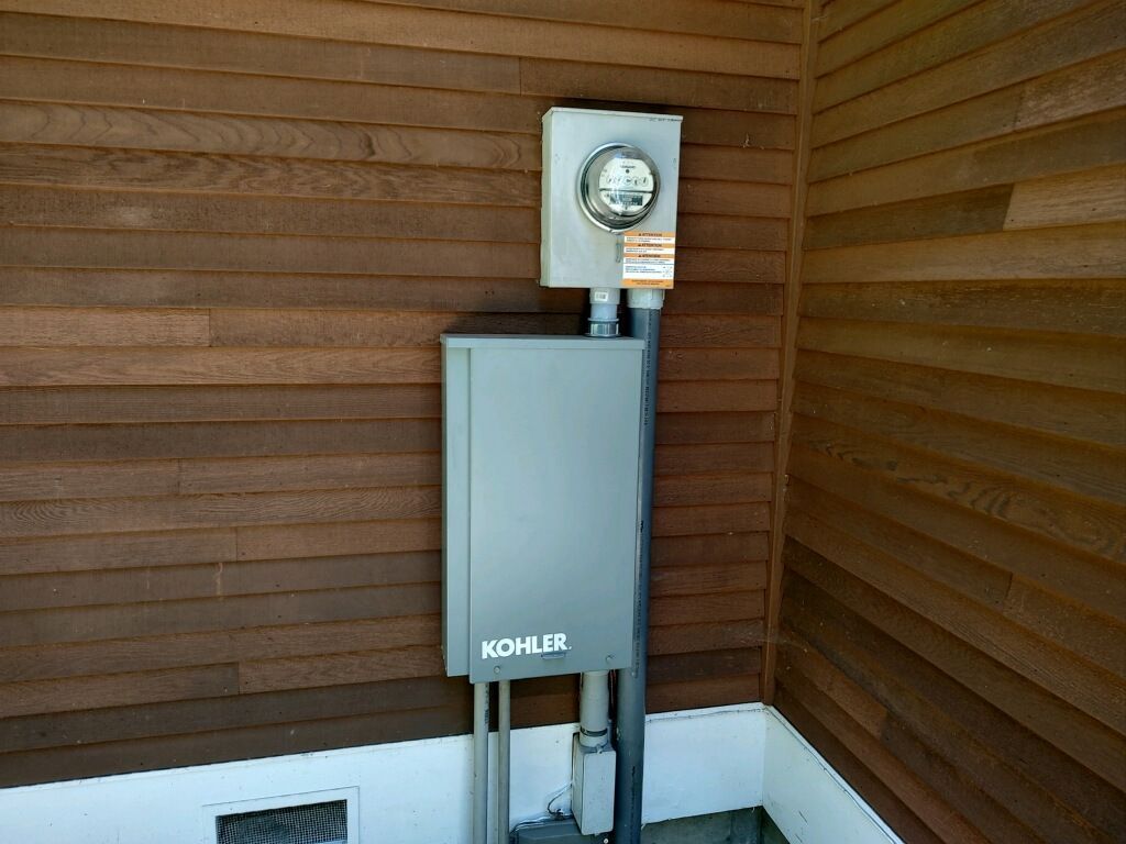 Electrical meter and gray box mounted on brown wood siding.