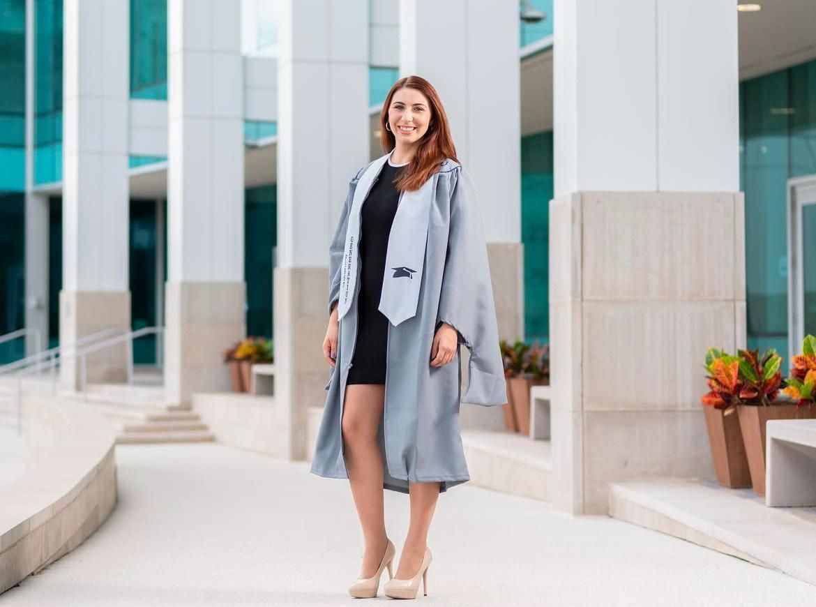 A woman in a graduation cap and gown is standing in front of a building.