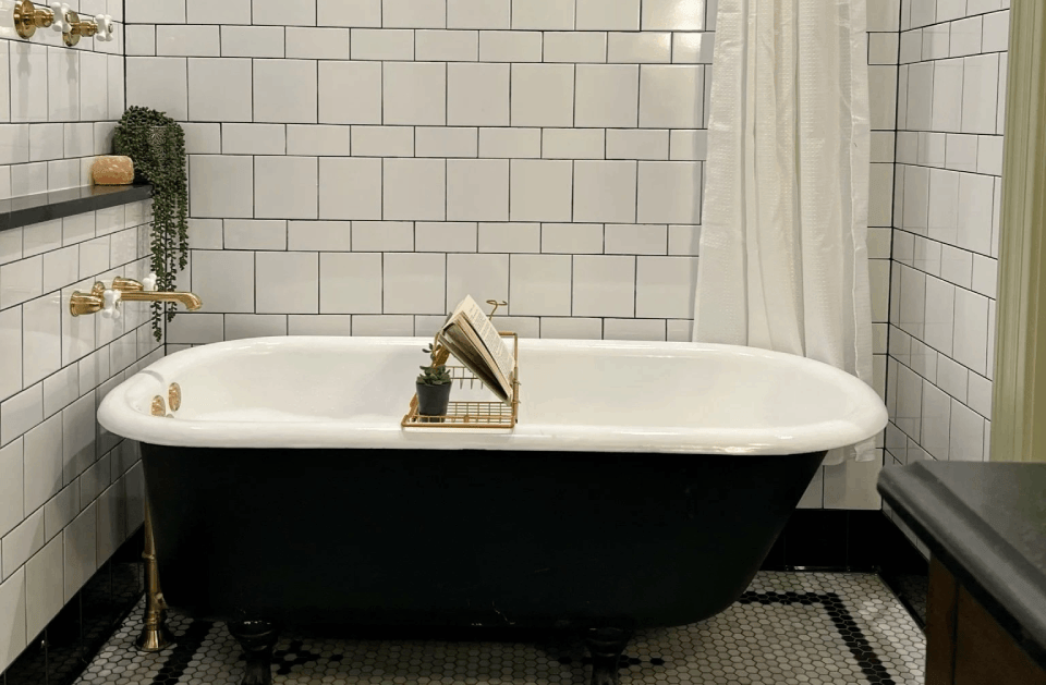 Modern bathroom with black-and-white clawfoot tub, white tile walls, and gold fixtures