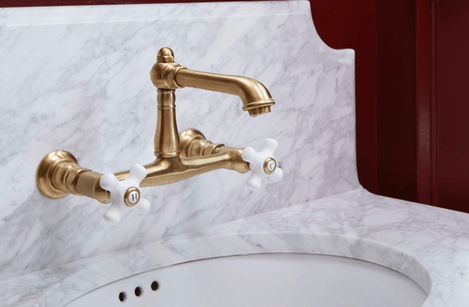 Brass bathroom faucet with white handles mounted on a marble sink backsplash