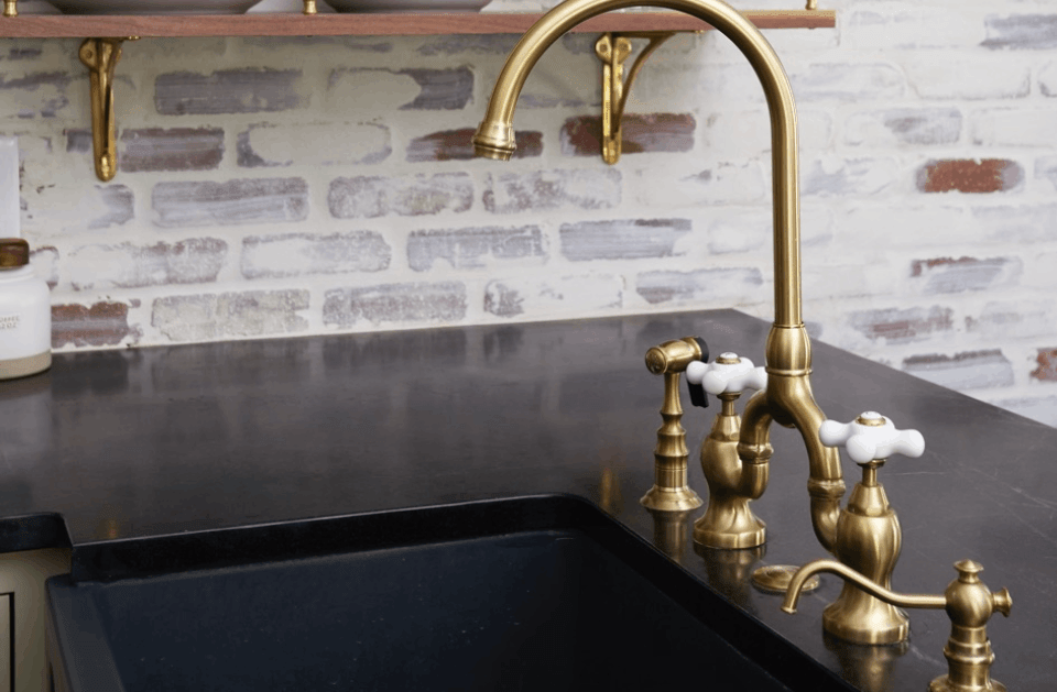 Brass faucet over a black kitchen sink against a white brick backsplash
