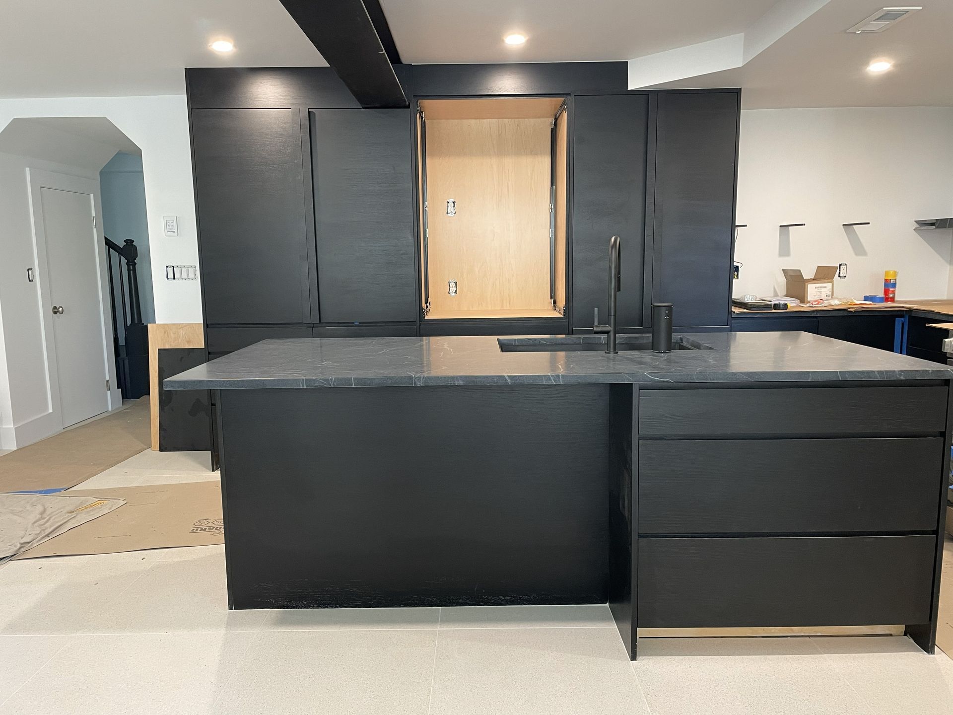 Modern kitchen with dark cabinets, black island, and a light wood pantry door under renovation
