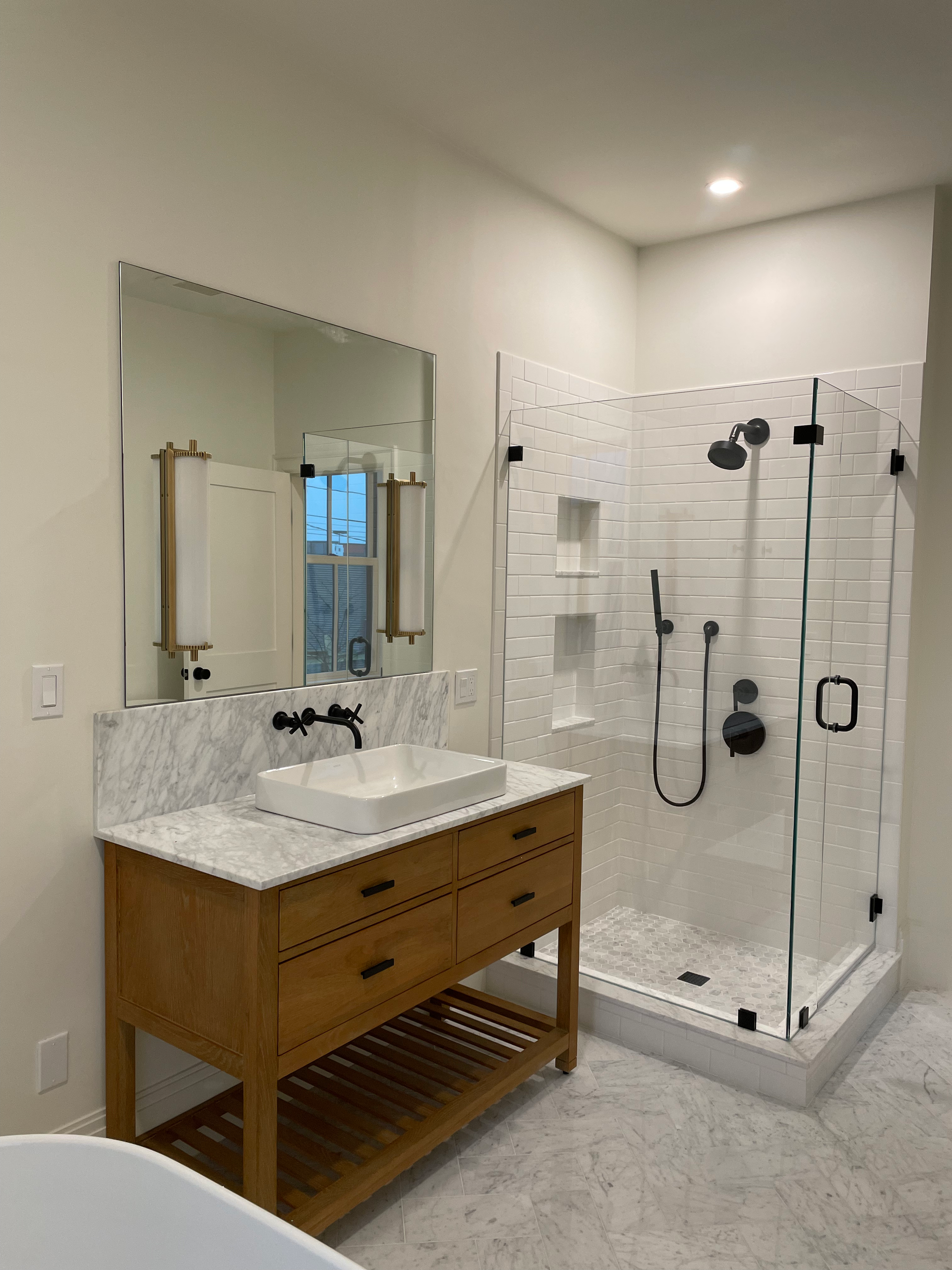 Bright bathroom with marble vanity, large mirror, and glass walk-in shower with black fixtures.
