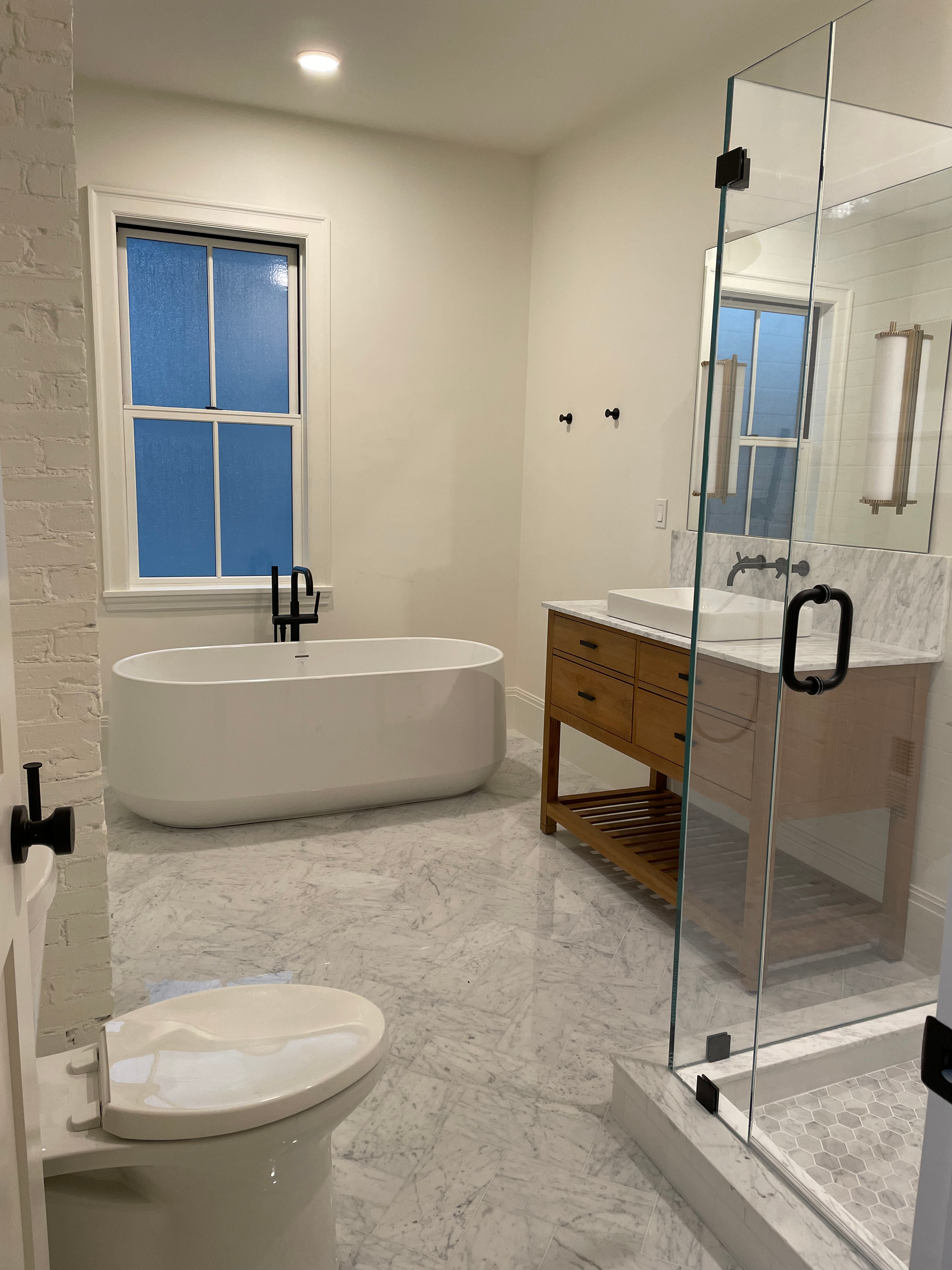 Modern bathroom with freestanding tub, toilet, glass shower, and wooden vanity