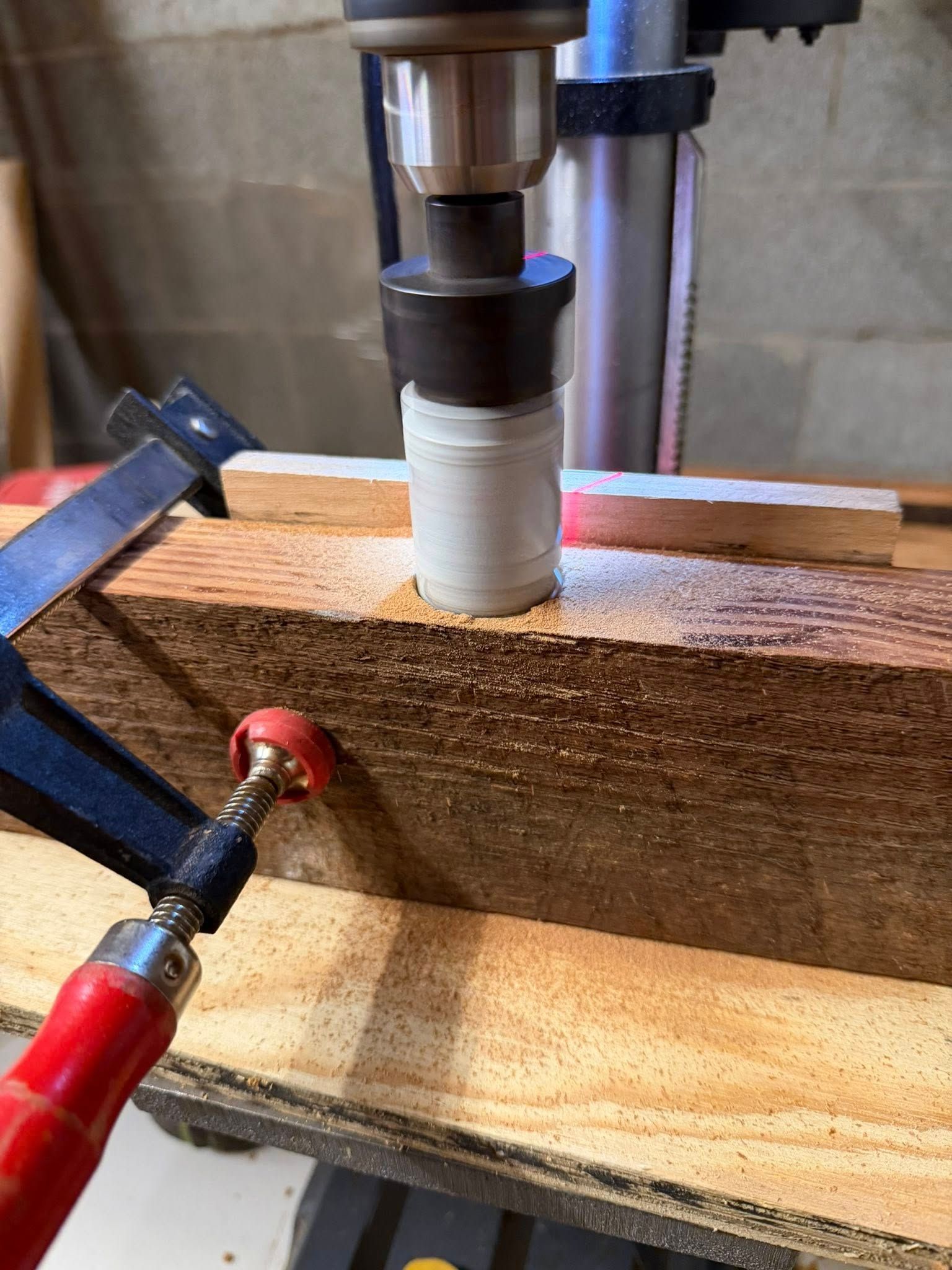 Drill press boring a hole into a wooden block clamped in place with a metal clamp.